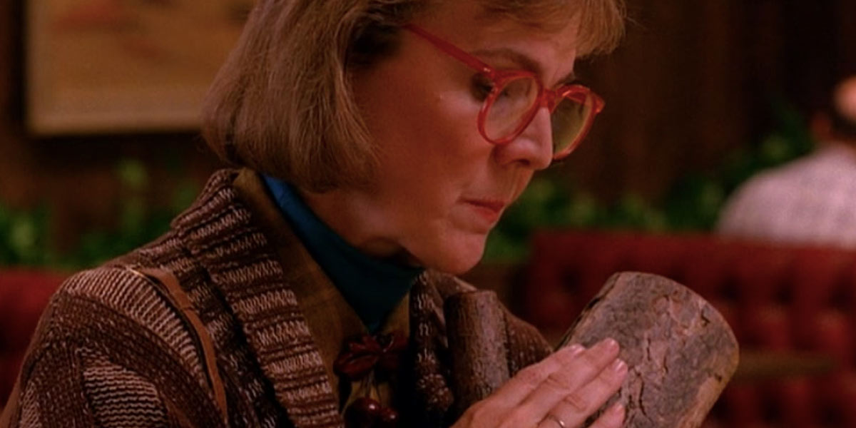 Still from the 1980s TV show Twin Peaks showing actress Catherine E. Coulson as the Log Lady stroking her pet log