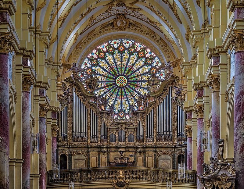 Interior photograph of a church showing the pipe organ facade below a large stained glass window